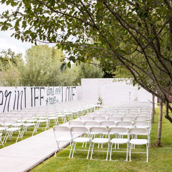 Outdoor wedding ceremony with white chairs along a fence with trees