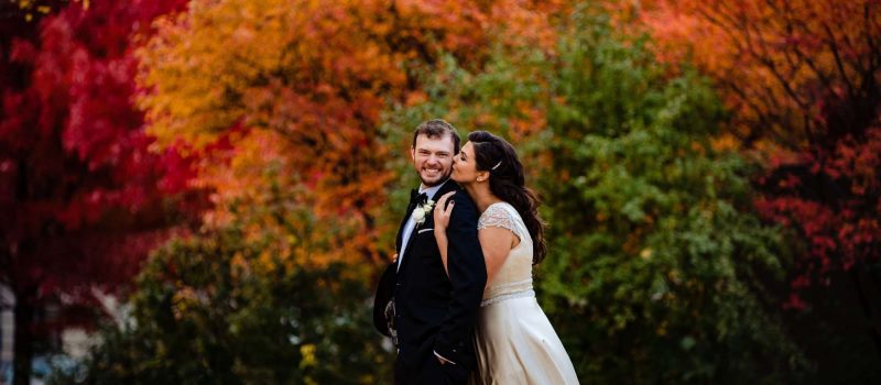 bride kisses groom by fall trees in Syracuse, NY