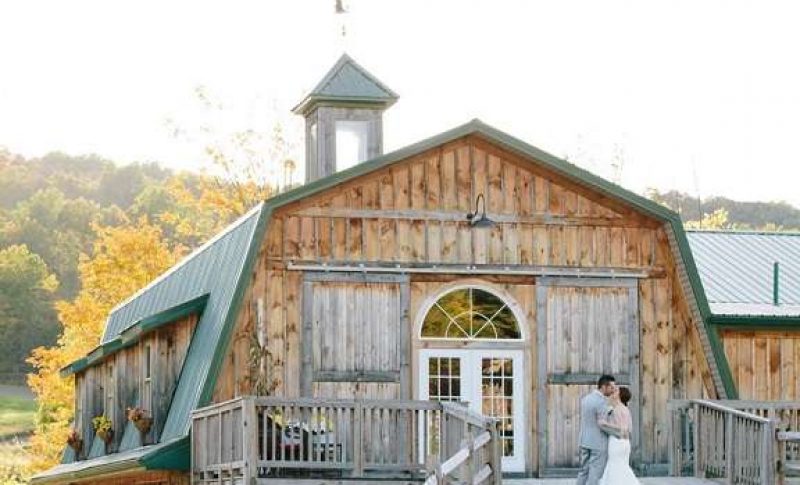bride and groom kiss beside brown barn with green roof